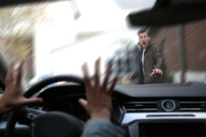 A pedestrian about to be hit by a car in a crosswalk.