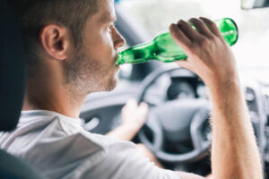 Drunk driver drinking behind the steering wheel of a car.