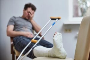 A sad man with a broken leg sits on a chair.